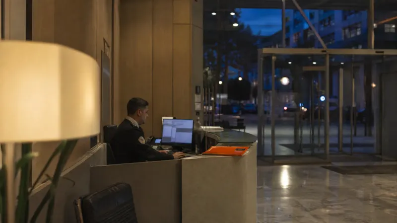 Portaria de um edifício de escritórios ao fim do dia, com o posto de vigilância iluminado